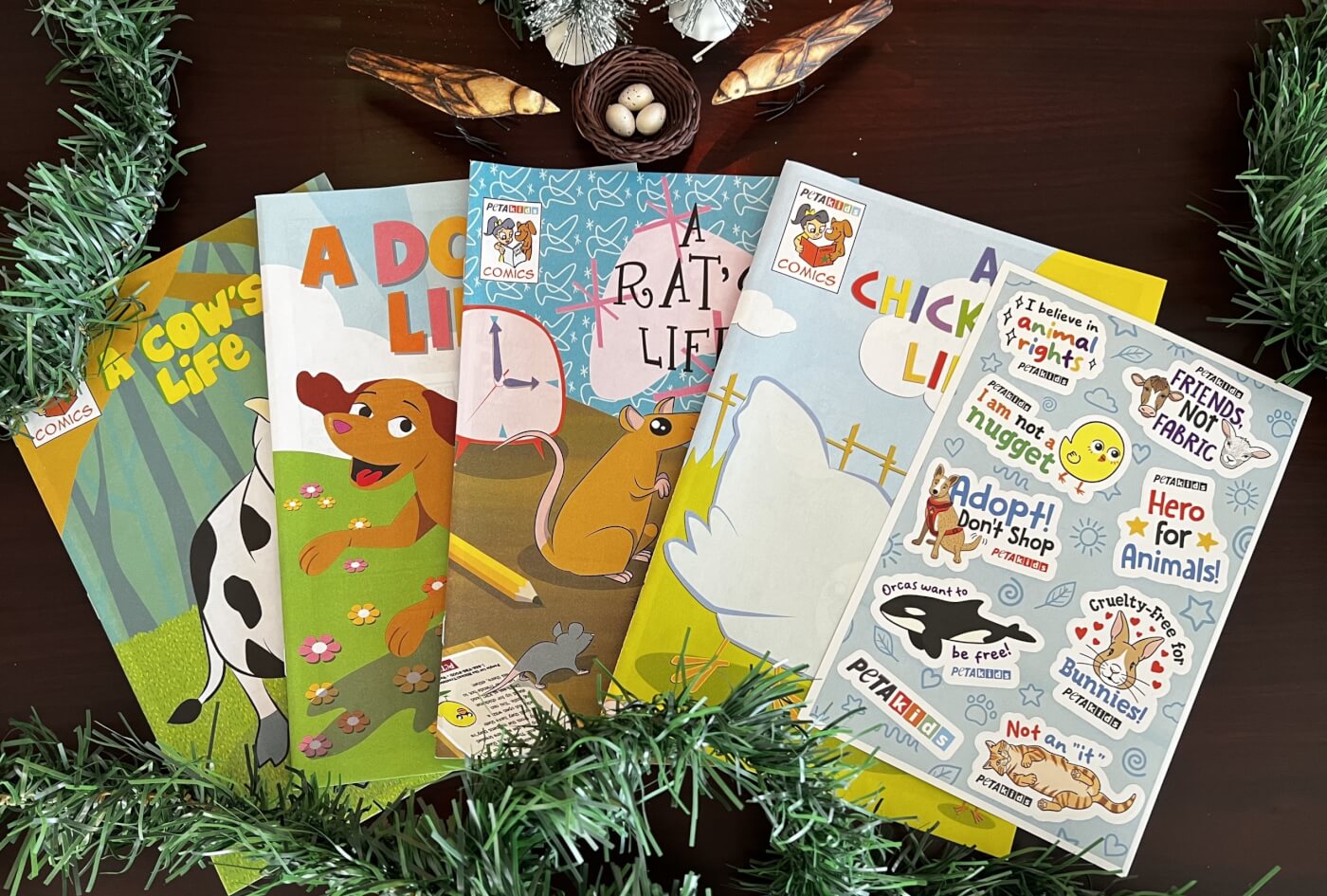 A display of PETA Kids comics on a dark wood table with holiday decorations