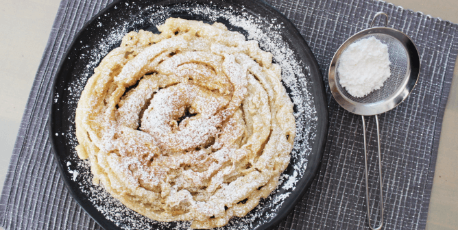 a vegan funnel cake topped with powdered sugar on a blue placemat