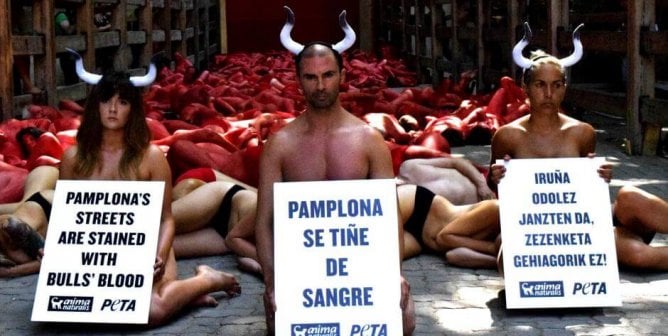 humans on the ground with signs and wearing horns to protest the Running of the Bulls