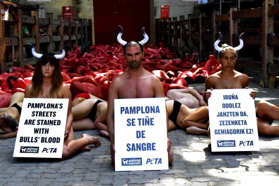 humans on the ground with signs and wearing horns to protest the Running of the Bulls