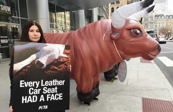 Inflatable bull and protester holding "Every Leather Car Seat Had a Face" sign