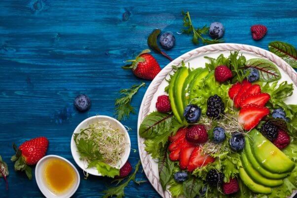 Salad with berries and avocados laid out on blue tabletop