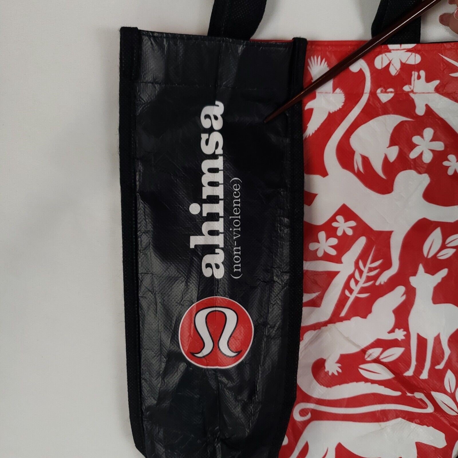 red and black lululemon shopping bag from 2012 that says "ahimsa", a word meaning nonviolence to living beings, on its side and shows silhouettes of various animals on its front