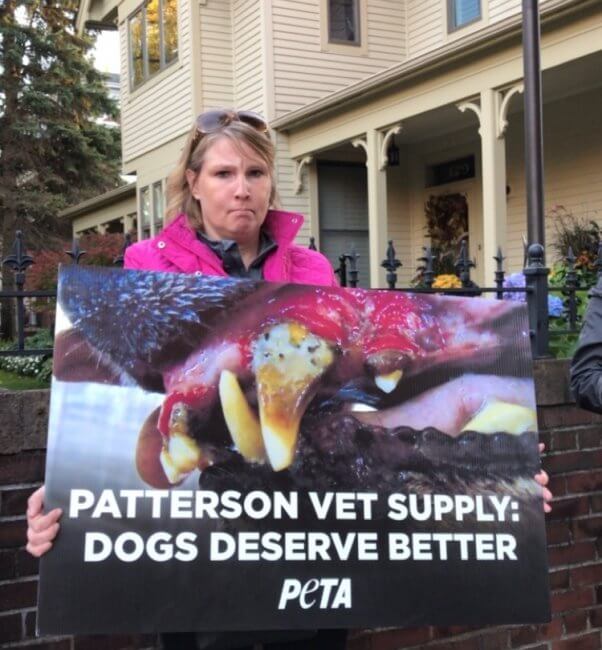 Woman in pink coat holding sign reading "Patterson Vet Supply: Dogs Deserve Better"