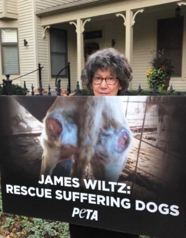 Woman holding sign reading "James Wiltz: Rescue Suffering Dogs"