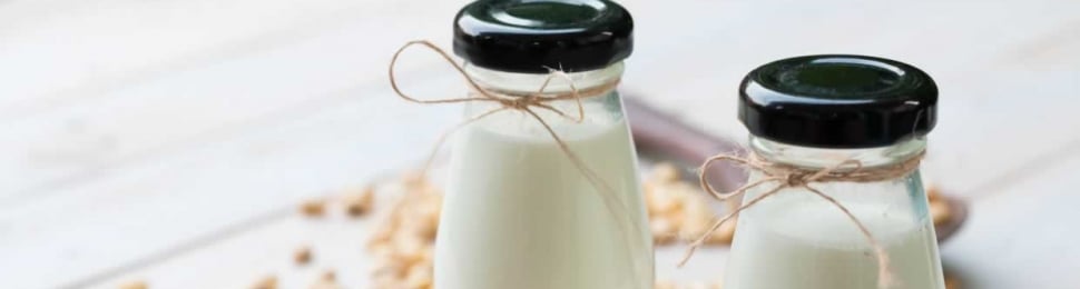 Two small bottles of fresh soymilk with soybeans scattered around base