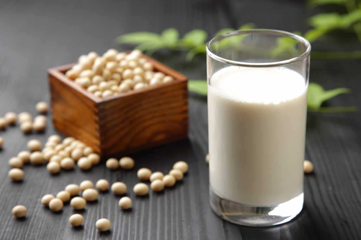 Glass of soymilk and small wooden container of soybeans