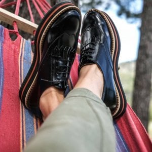 someone wearing shiny vegan black dress shoes while in a hammock