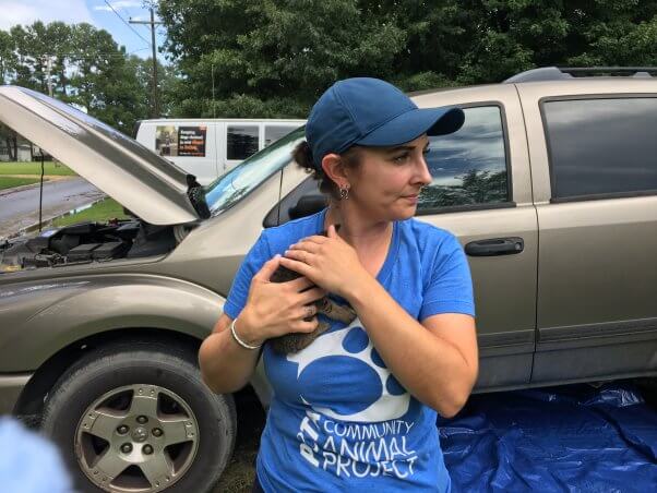 Woman in blue shirt and hat comforting kitten