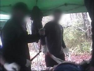 Two anonymous people stand over a goat.