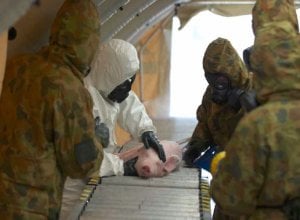 A group of anonymous people stand over a small pig on a grate. All of the people are wearing masks.