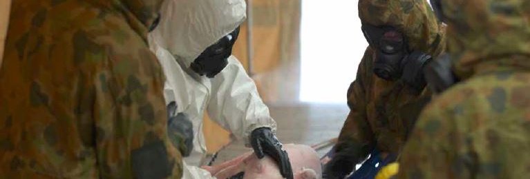 A group of anonymous people stand over a small pig on a grate. All of the people are wearing masks.