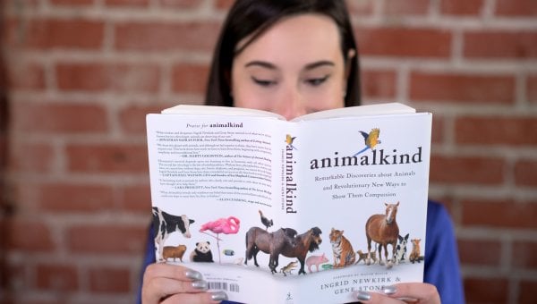 woman reads animalkind by ingrid newkirk against a brick wall