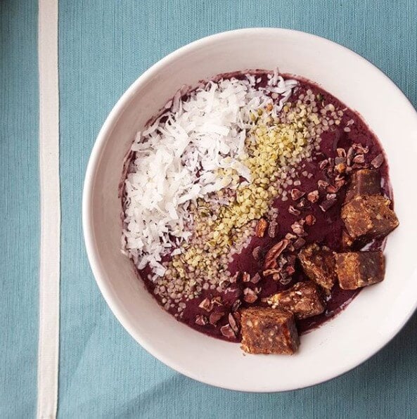 blueberry smoothie bowl topped with coconut, seeds, chocolate lara bar