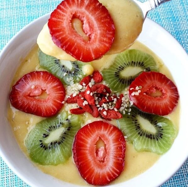 orange mango smoothie bowl topped with strawberries and kiwi