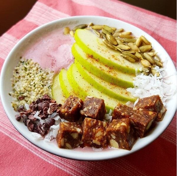 strawberry smoothie bowl topped with sliced apples, seeds, and apple pie lara bar