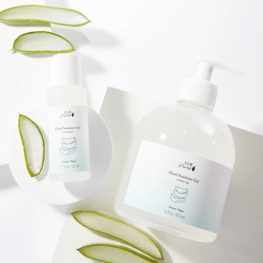 100% Pure brand gel hand sanitizer in two sizes on a white background with slices of aloe vera
