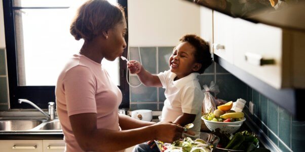 Baby feeding mother who is preparing vegetables