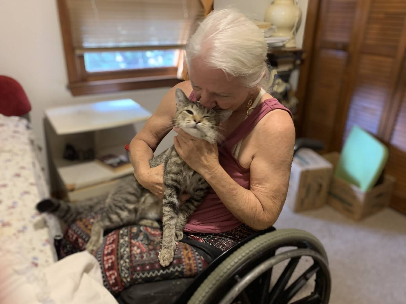 A woman in a wheelchair cuddling a grey cat