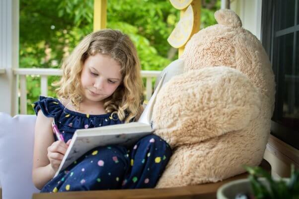 Young blond girl reads next to teddy bear