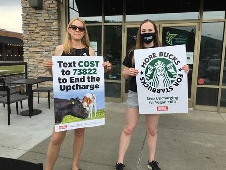 2 students hold signs protesting the additional charge for Vegan milk at Starbucks