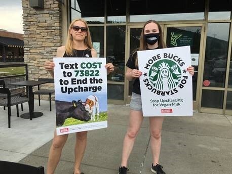 2 students hold signs protesting the additional charge for Vegan milk at Starbucks