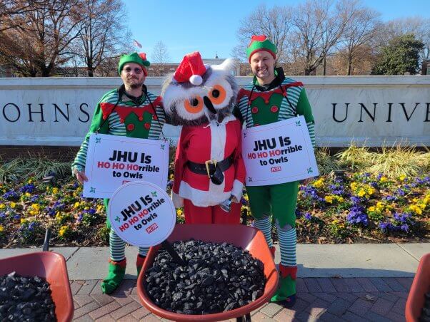 PETA activists in owl and elf costumes pose with a wheelbarrow full of coal for JHU president