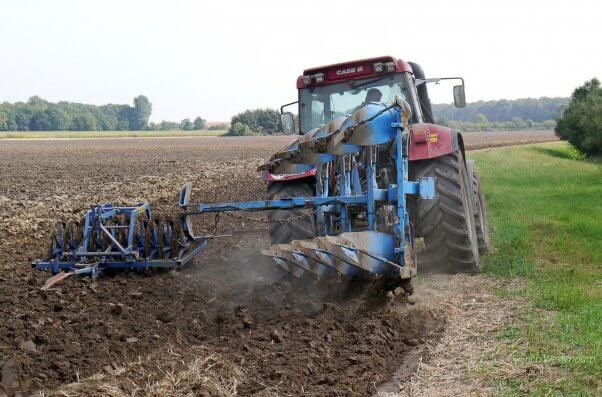 A huge tractor plows through a field, churning the soil