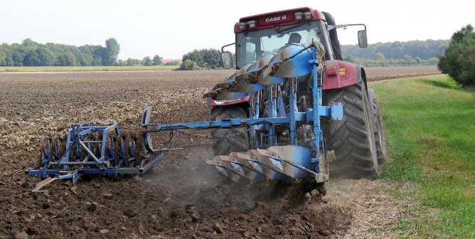 A huge tractor plows through a field, churning the soil