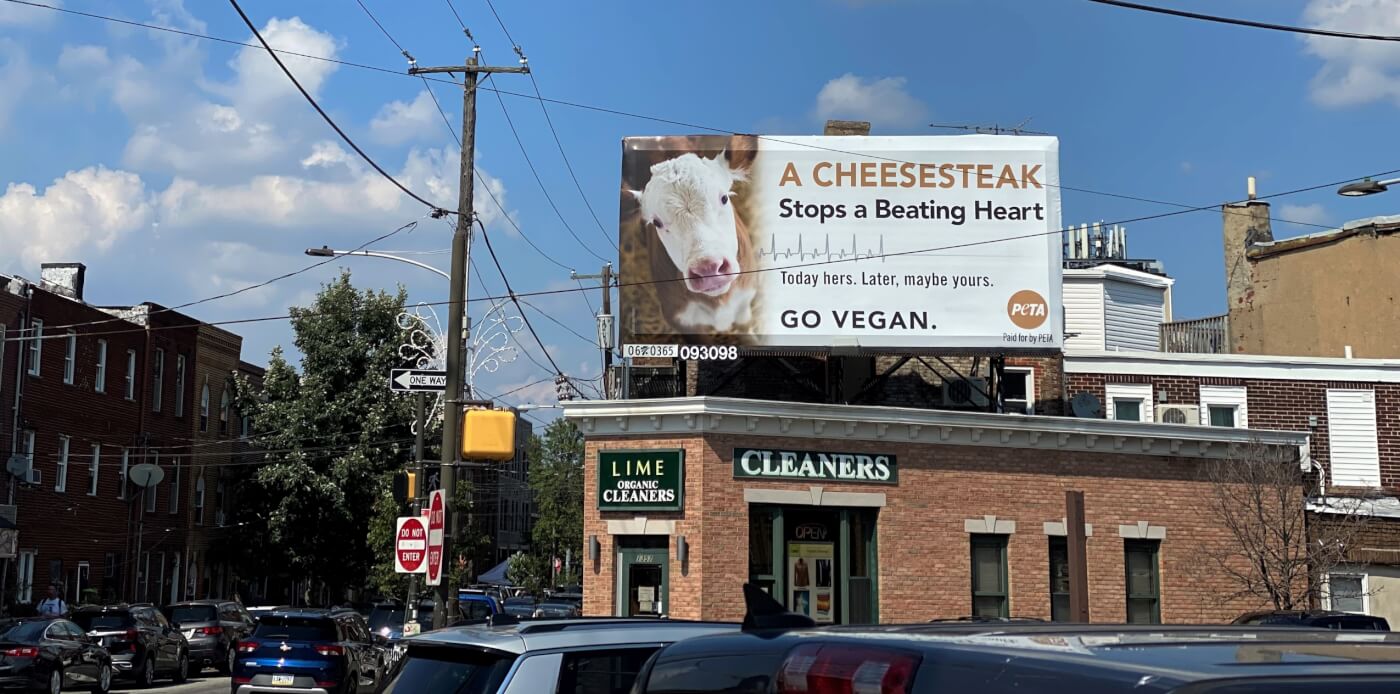 A billboard in Philadelphia, PA featuring a cow reads "A cheesesteak stops a beating heart. Today hers. Later, maybe yours. Go vegan."