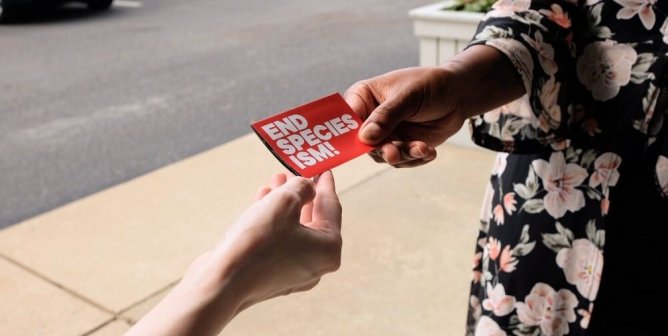 A person hands an End Speciesism sticker to another person