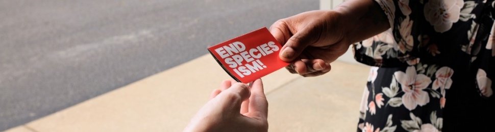 A person hands an End Speciesism sticker to another person