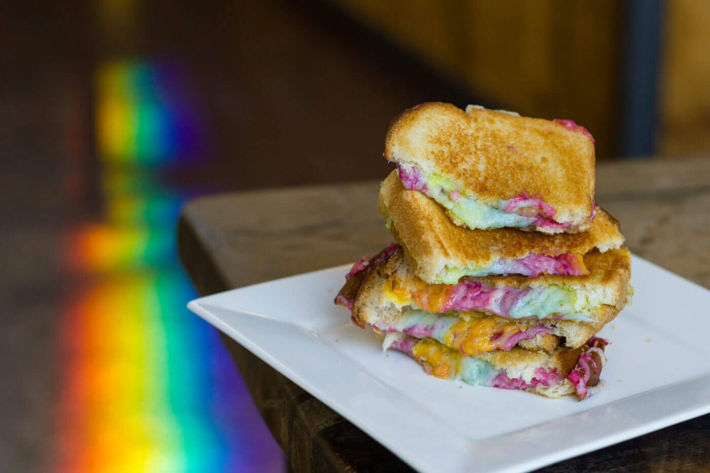 vegan rainbow grilled cheese sandwich stacked on a plate with a real rainbow in the background
