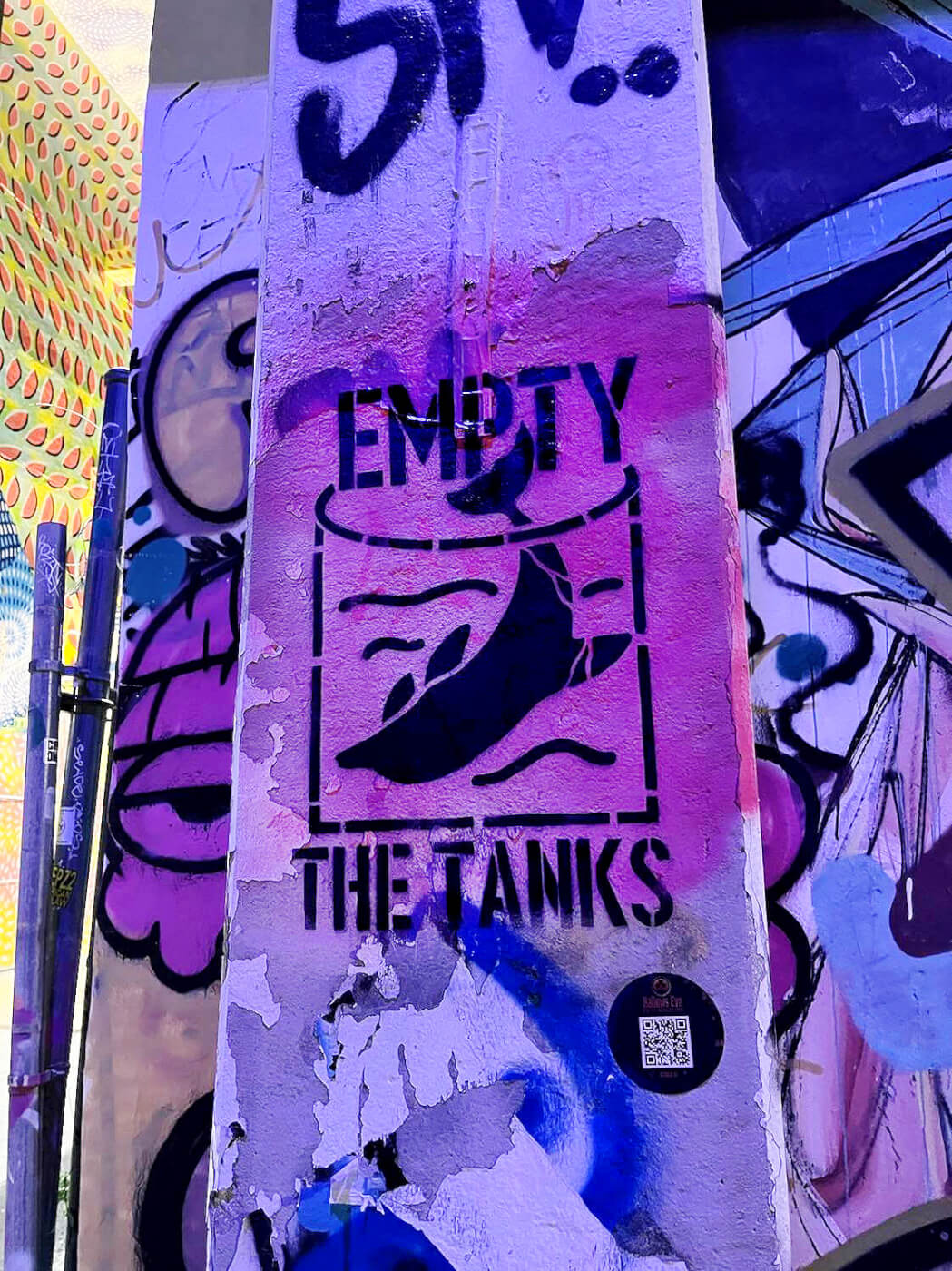 stenciled spray paint art on a concrete pole reading "empty the tanks" with an illustration of a dolphin in a small tank.