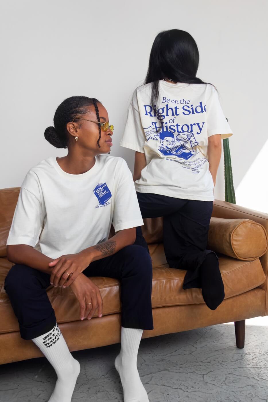 women wearing the peta sos don't eat the homies collab tshirt which is white with blue lettering and says "be on the right side of history" with a graphic of a boy and a girl reading a book about human history