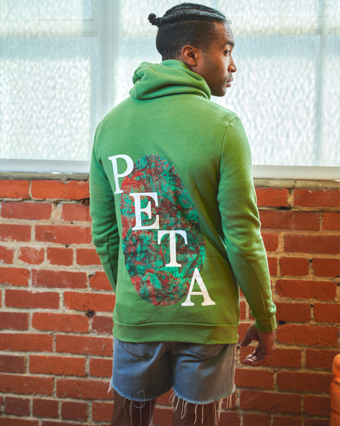A model stands with their back to the camera and their face in side profile view, the back of their green sweatshirts says "PETA"