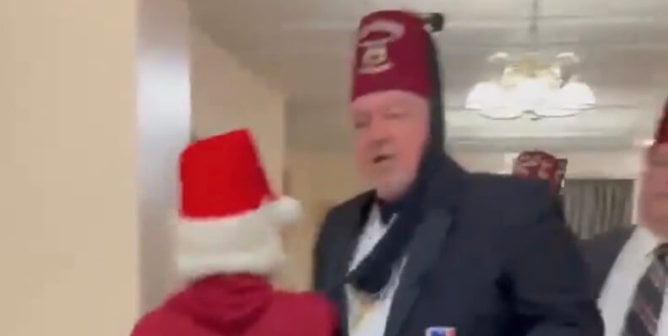 A peaceful protestor dressed as Santa is blocked from the exit of the Moolah Shrine by a tall person wearing a fez.