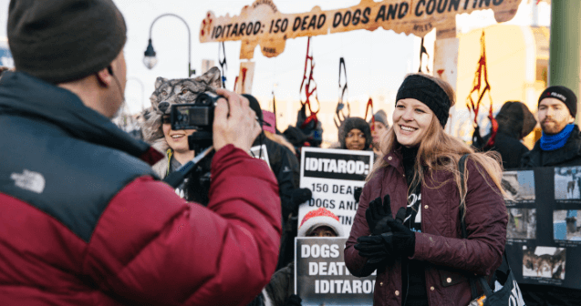 Person gives interview in front of Iditarod protest