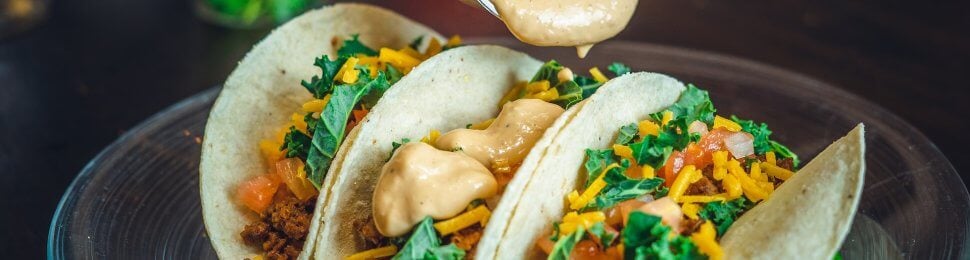 vegan taco trio on a plate with sauce being poured on