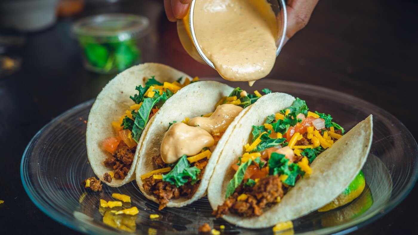 vegan taco trio on a plate with sauce being poured on What Happens to Your Body When You Go Vegan?
