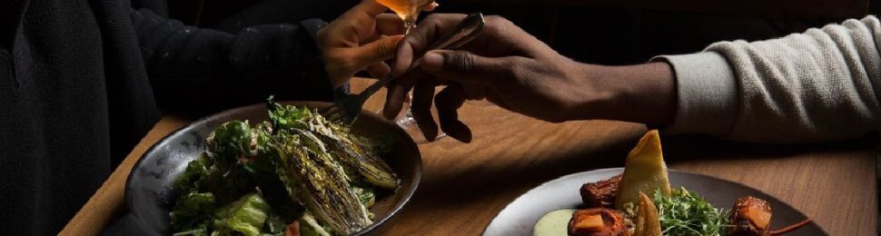 food on a table at a romantic vegan restaurant with the arms of two people reaching across