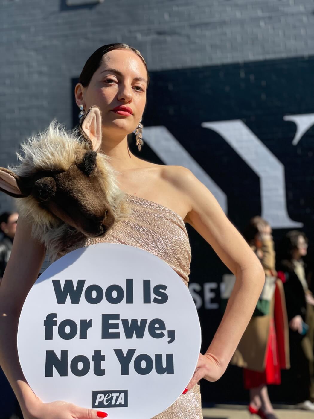 NY Fashion Week PETA demo model wearing a Schiaparelli-esque "sheep" dress and holding a sign promoting wool-free designs
