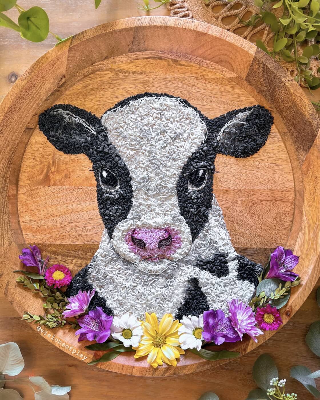 black and white cow made of rice surrounded by flowers on a wooden plate