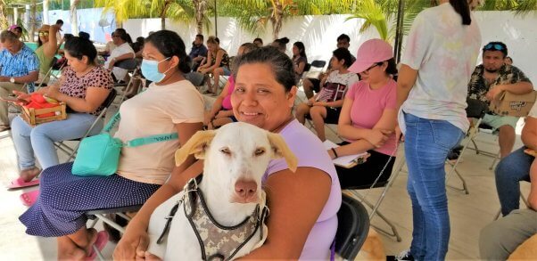 mujer con perro blanco en arnés espera con otros en sillas para esterilizar/castrar evento en Cancún para perros y gatos