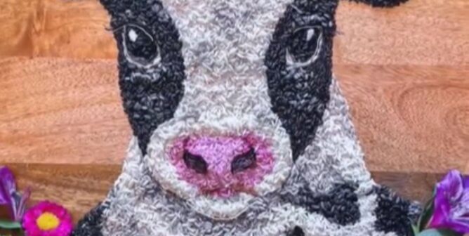 close-up of a black and white cow made of rice surrounded by flowers on a wooden plate