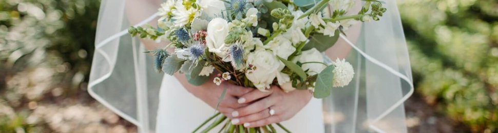 A bride in a white dress and veil holds a bouquet of flowers