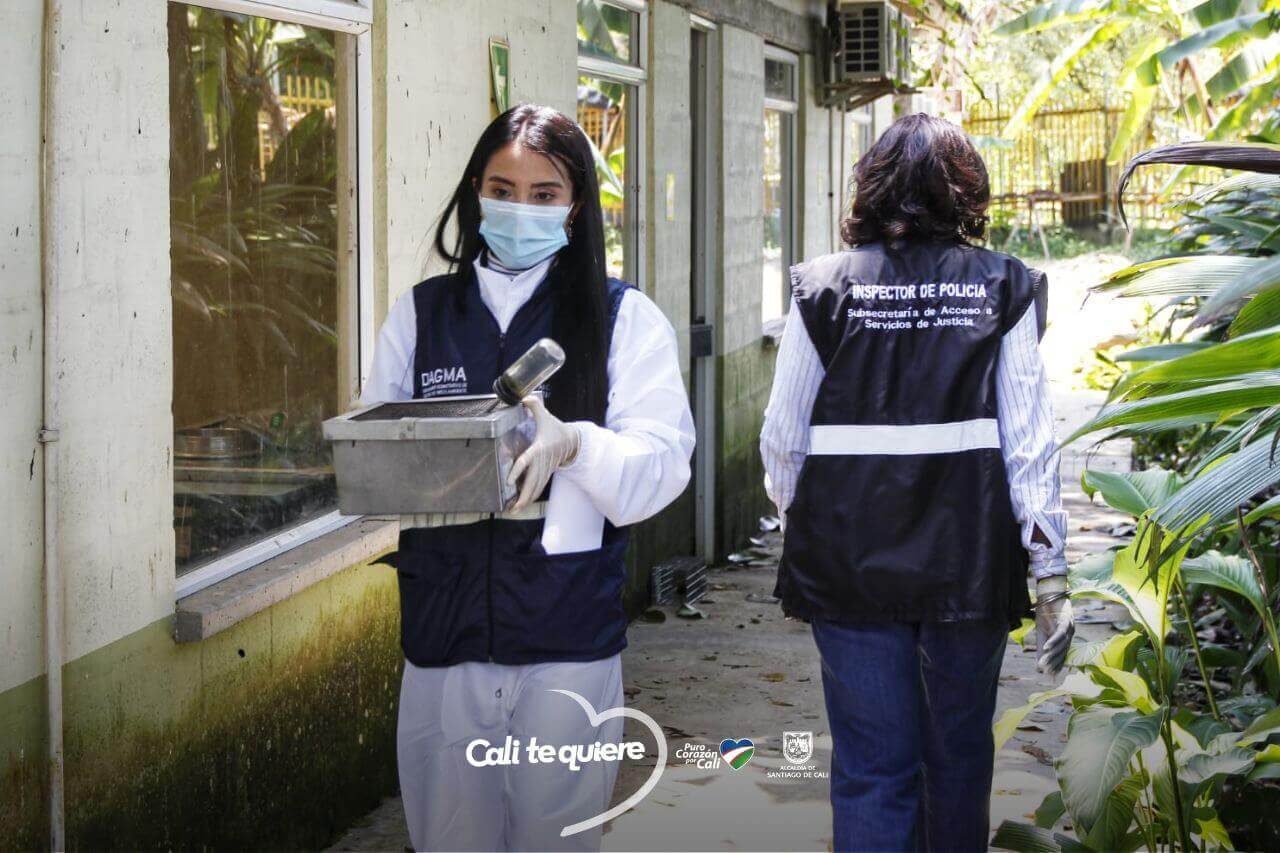 two workers passing each other outside the caucaseco laboratory. their vests read "Inspector de Policia: Subsecretaria de acceso a Servicios de Justicia"