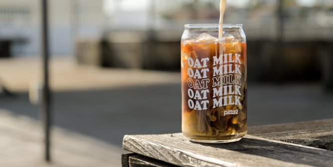 someone pouring oat milk into coffee