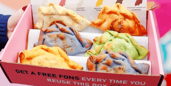 a person is holding a pink box with multi-colored vegan empanadas