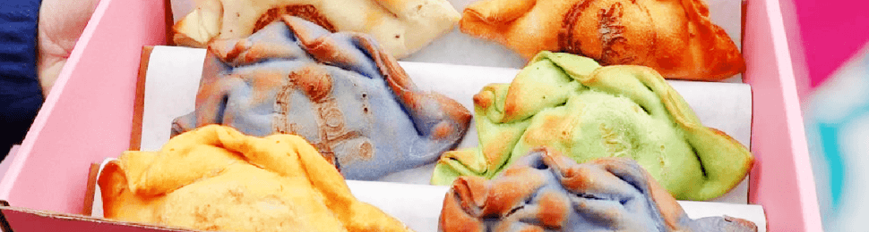 a person is holding a pink box with multi-colored vegan empanadas